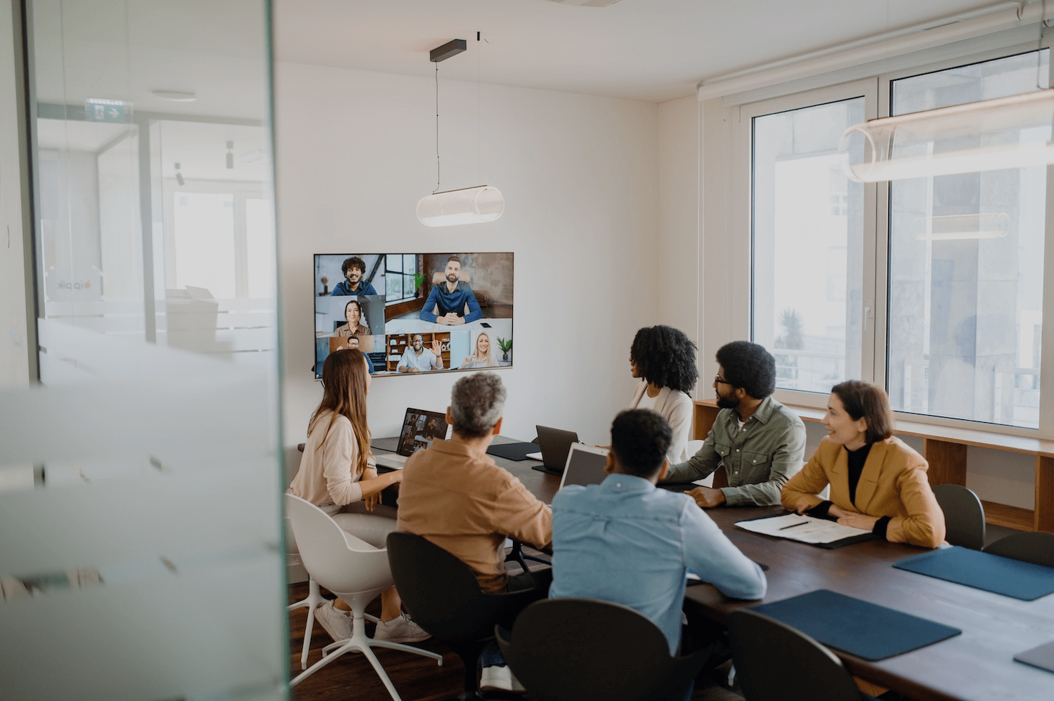 A diverse group of professionals in a conference room participates in a video conference call with a remote team